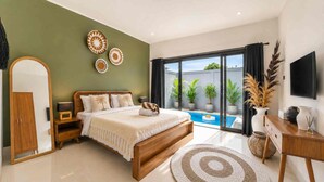 A bedroom with a bed, a nightstand, a mirror, a TV, a desk, and a view of a swimming pool. - Bella Vita Villa (Kerobokan)