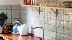 Una cocina con encimera de madera, un lavabo y estantes con platos y vasos.