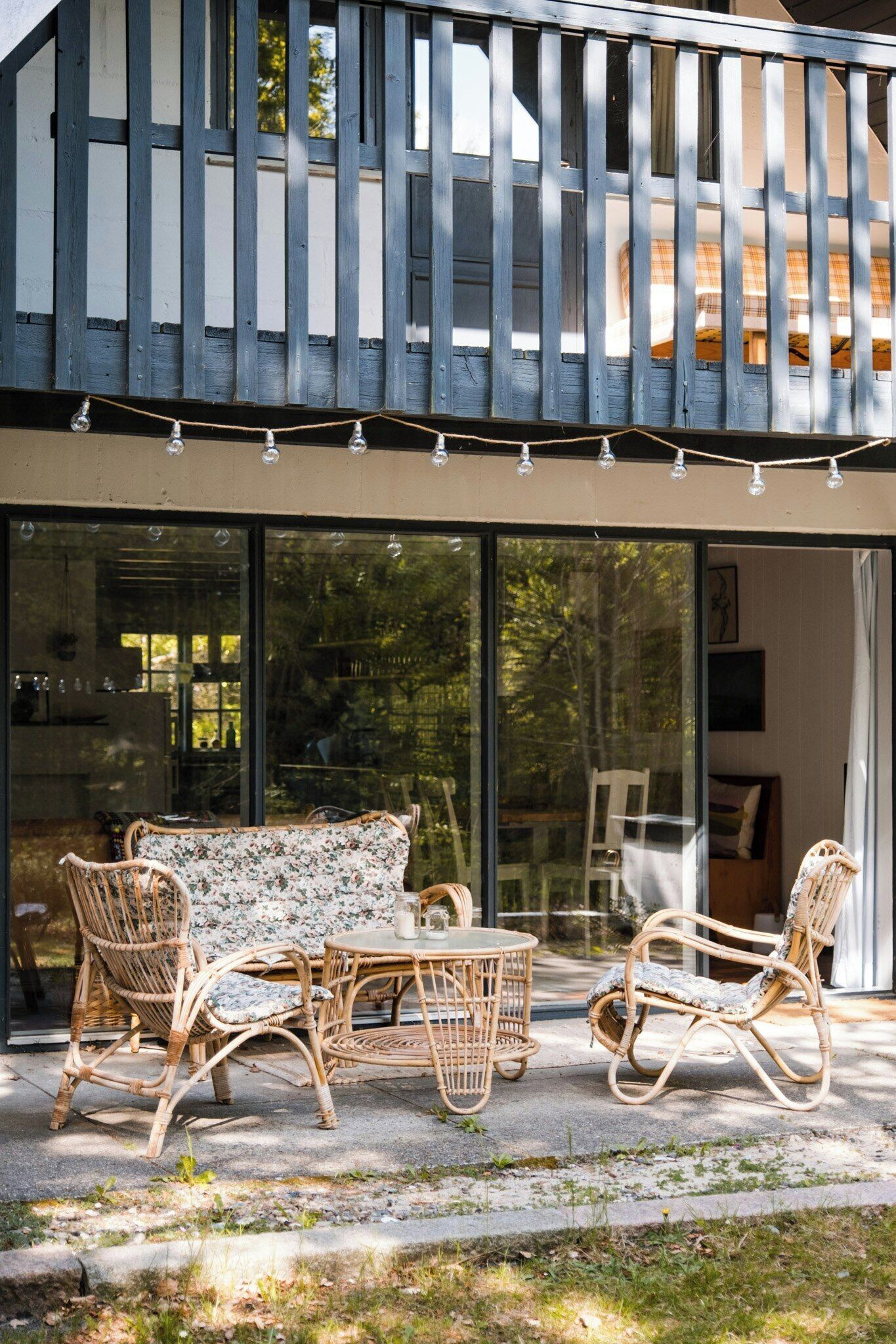 A modern outdoor seating area with wicker furniture, a glass door entrance, and a balcony with a railing.