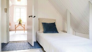 Un dormitorio con una cama, una puerta, una ventana y una mesita con una planta.