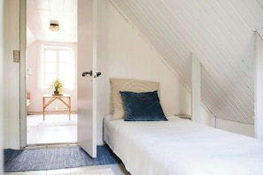 Ein Schlafzimmer mit Bett, Tür, Fenster und einem kleinen Tisch mit Pflanze.