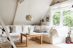 A white loft bedroom with a sloped ceiling, a wooden table, a white sofa, and a large window with a view of greenery. - Close to beach, forest and bike trails (Grenå)