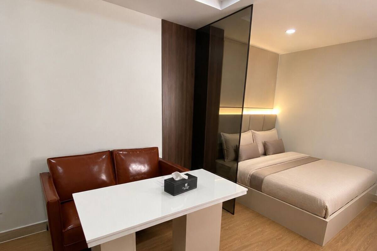 Ein modernes Zimmer mit einer braunen Ledersofa, einem weißen Tisch mit Taschentuchbox und einem Bett mit beigefarbener Bettwäsche, sowie einem Holzboden.