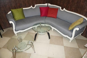 A curved sofa with a glass coffee table and metal legs, a patterned floor, and a dark wooden wall.