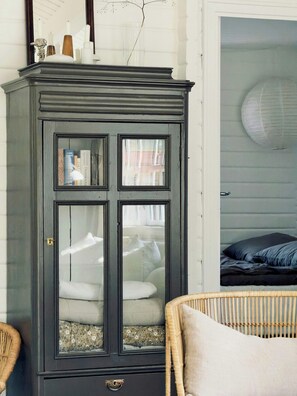 Ein dunkler Holzschrank mit Glastüren, ein Korbstuhl und ein Bett mit gestreifter Bettdecke.