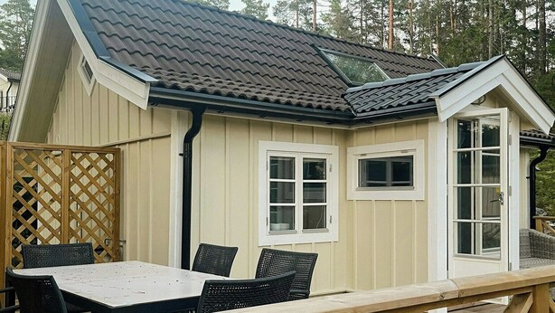 Eine Holzterrasse mit Tisch und Stühlen, ein kleines Gebäude mit geneigtem Dach und ein Holzzaun.