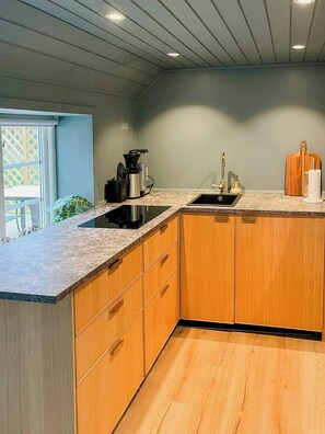 A modern kitchen with a built-in stove, sink, and wooden cabinets. - Cabin with private beach at Ingarö (Ingarö)