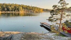Ein See mit einem Steg, der ins Wasser führt, umgeben von Bäumen und einem roten Gebäude.