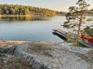 A lake with a dock extending into the water, surrounded by trees and a red building. - Cabin with private beach at Ingarö (Ingarö)