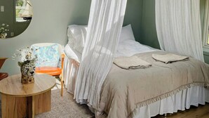 Ein Schlafzimmer mit einem Himmelbett, einem runden Holztisch mit einer Vase und einem Stuhl mit einem Blumenkissen.