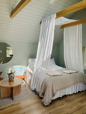 A bedroom with a four-poster canopy bed, a round wooden table with a vase, and a chair with a floral cushion. - Cabin with private beach at Ingarö (Ingarö)