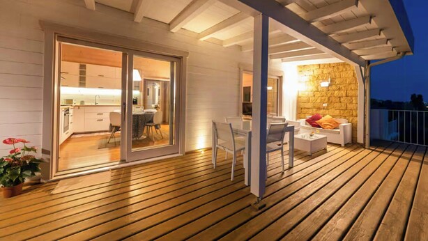 An outdoor deck with a wooden floor, a dining area with a table and chairs, and a kitchen visible through a glass door. - House with pool and citrus grove near Noto (Noto)