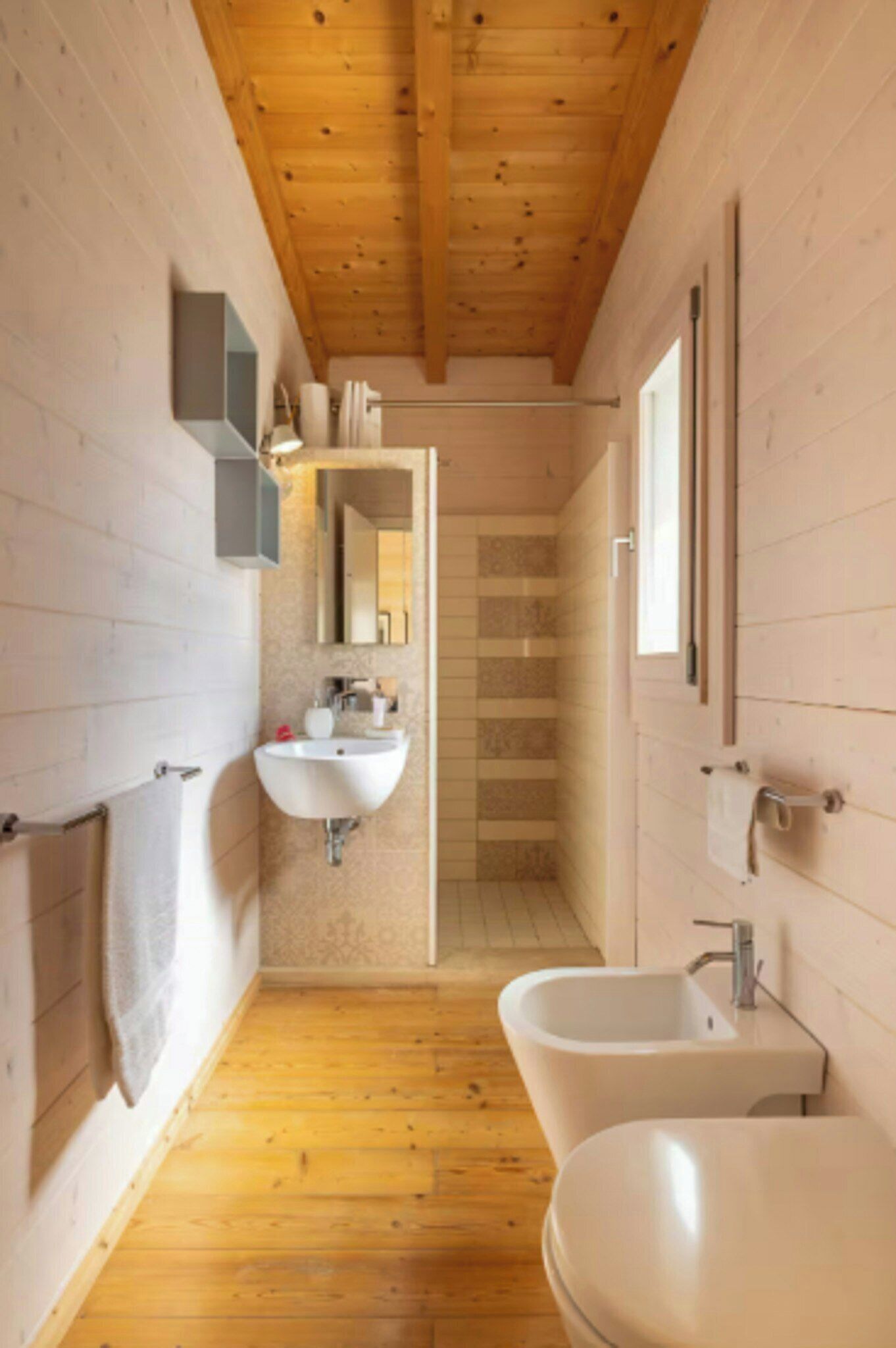 A modern bathroom with wooden flooring, a sink, a bidet, and a shower.