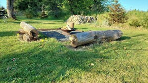 A natural outdoor setting with a fire pit surrounded by logs and rocks. - Retro guest house near Rebild Hills (Hadsund)