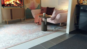 A living room with a television displaying a fire, a sofa, a small table with a cup, a patterned rug, and a pine cone decoration. - Retro guest house near Rebild Hills (Hadsund)
