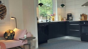 A modern kitchen with black cabinets, a dishwasher, a coffee maker, and a window with a view of greenery. - Retro guest house near Rebild Hills (Hadsund)