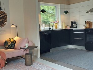 Eine moderne Küche mit schwarzen Schränken, einem Geschirrspüler, einer Kaffeemaschine und einem Fenster mit Blick ins Grüne.