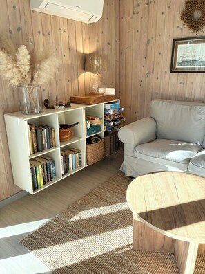 Ein Wohnzimmer mit einem weißen Sofa, einem Holztisch, einem Bücherregal und einer Wand-Klimaanlage.
