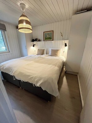 Ein Schlafzimmer mit einem großen Bett, einer Hängelampe, einem Bild an der Wand und einem Fenster.