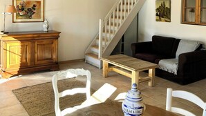 A spacious living area with a wooden staircase, a dining table with chairs, a sofa, and a decorative vase. - Unique gite in a renovated factory in Provence (Salernes)