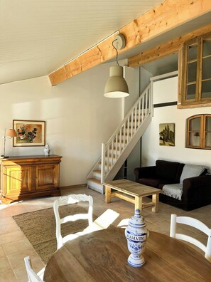 A spacious living area with a wooden staircase, a dining table with chairs, a sofa, and a decorative vase. - Unique gite in a renovated factory in Provence (Salernes)