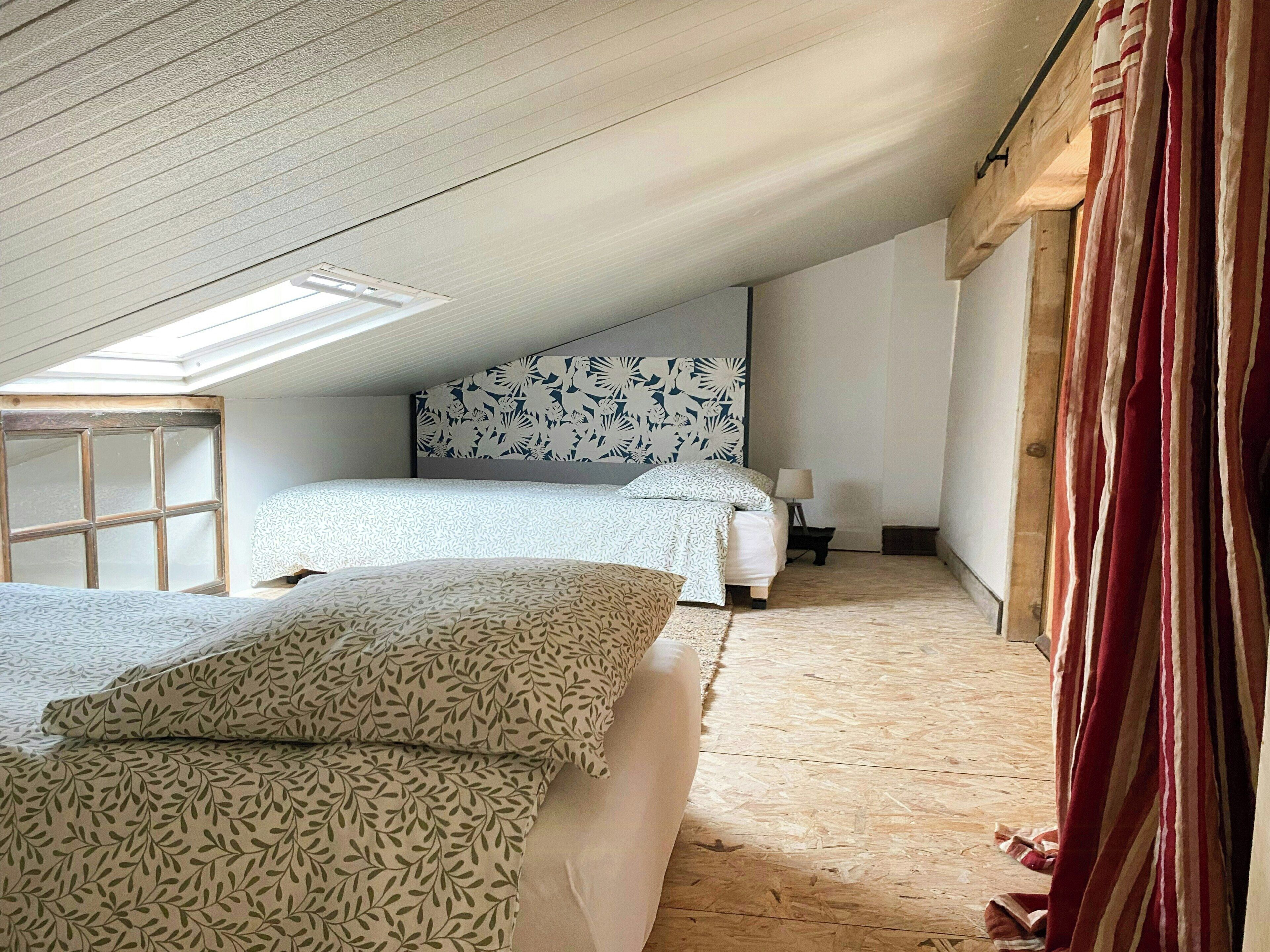 A bedroom with two beds, a skylight, a patterned headboard, and a wooden floor.