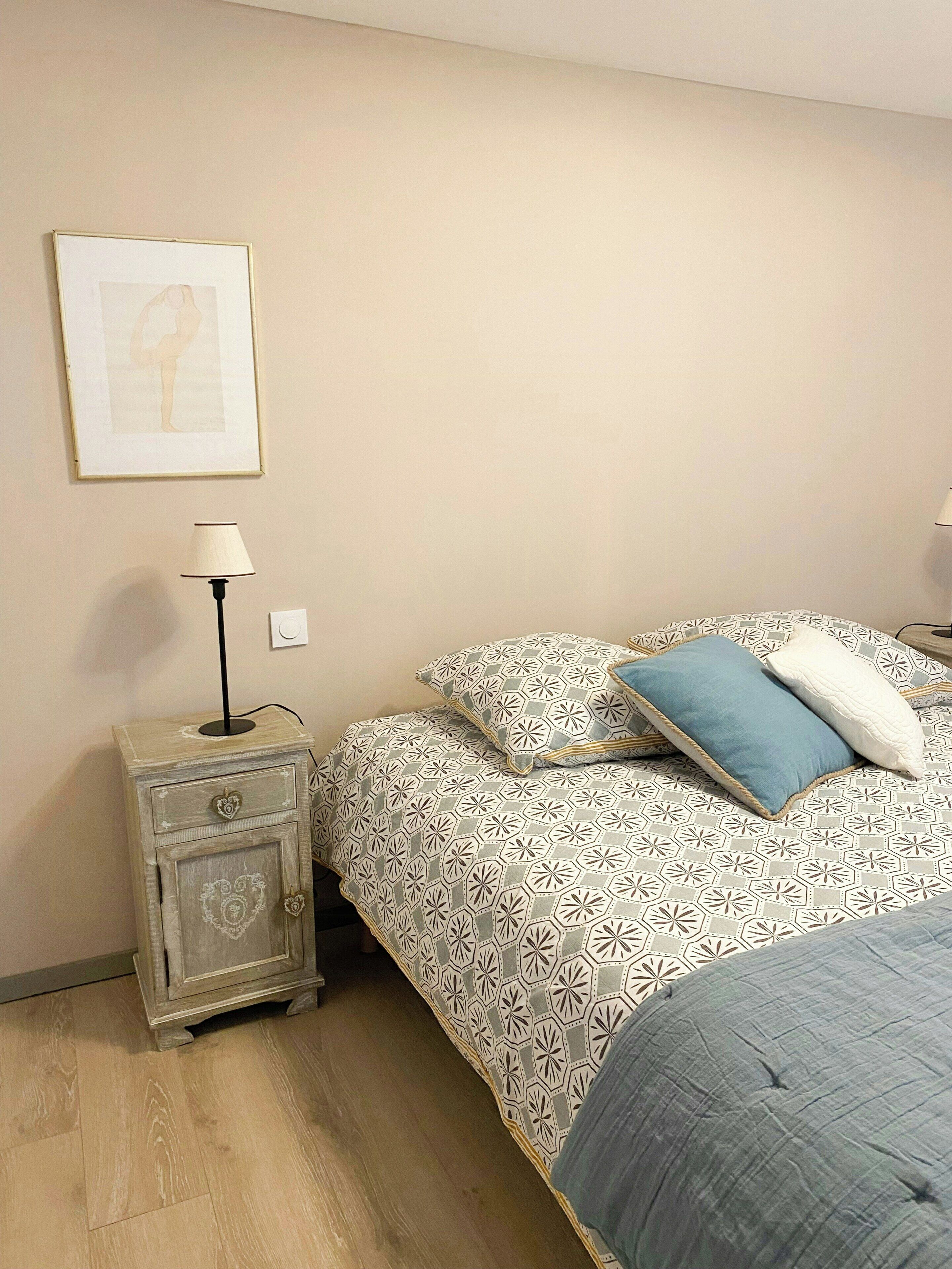 Une chambre à coucher avec un lit, une table de chevet avec une lampe, un tableau accroché au mur et une couvre-lit à motifs.