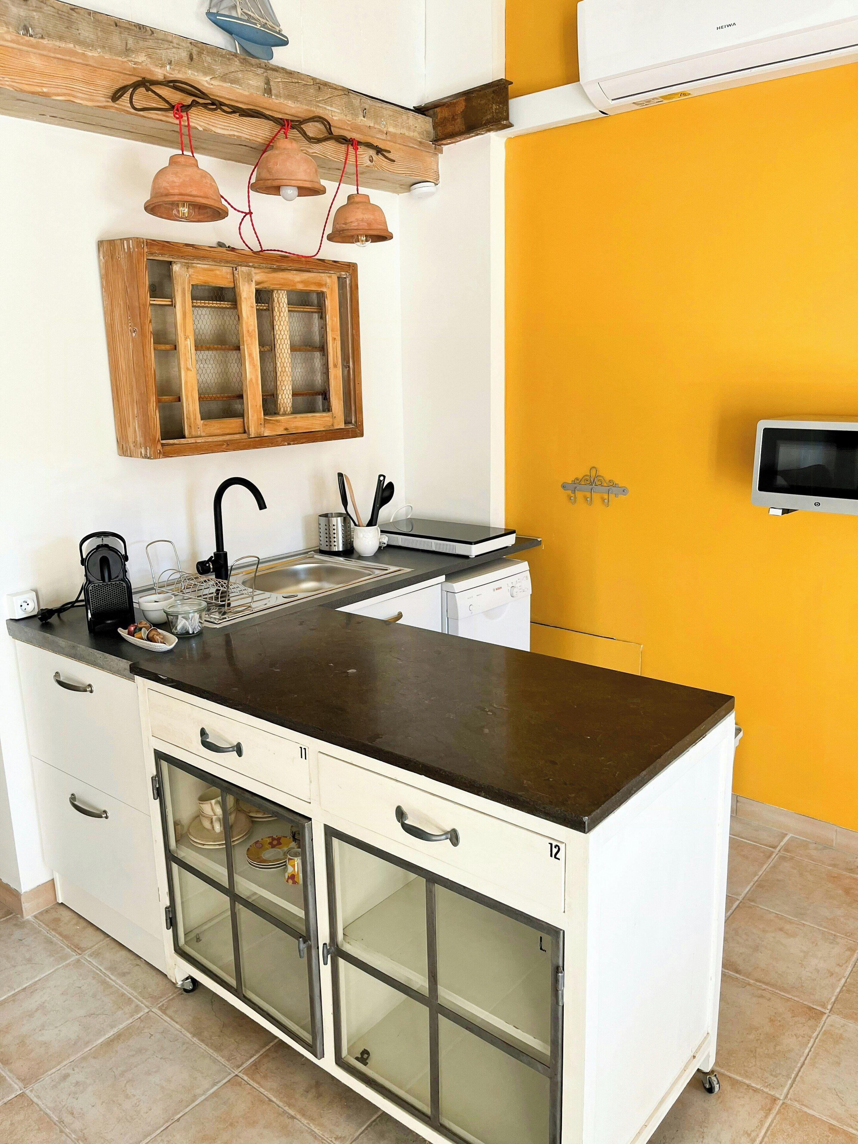 A kitchen with a black countertop, white cabinets, a wooden hanging light fixture, and a microwave.