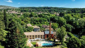 A rural area with a large building featuring a tall chimney, surrounded by trees and a swimming pool. - Unique gite in a renovated factory in Provence (Salernes)