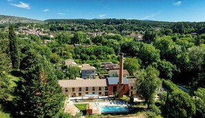 A rural area with a large building featuring a tall chimney, surrounded by trees and a swimming pool. - Unique gite in a renovated factory in Provence (Salernes)