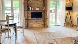 A room with a stone fireplace, a television, a dining table with chairs, and a tripod lamp. - Unique gite in a renovated factory in Provence (Salernes)