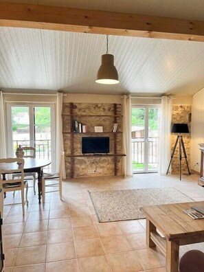 A room with a stone fireplace, a television, a dining table with chairs, and a tripod lamp. - Unique gite in a renovated factory in Provence (Salernes)