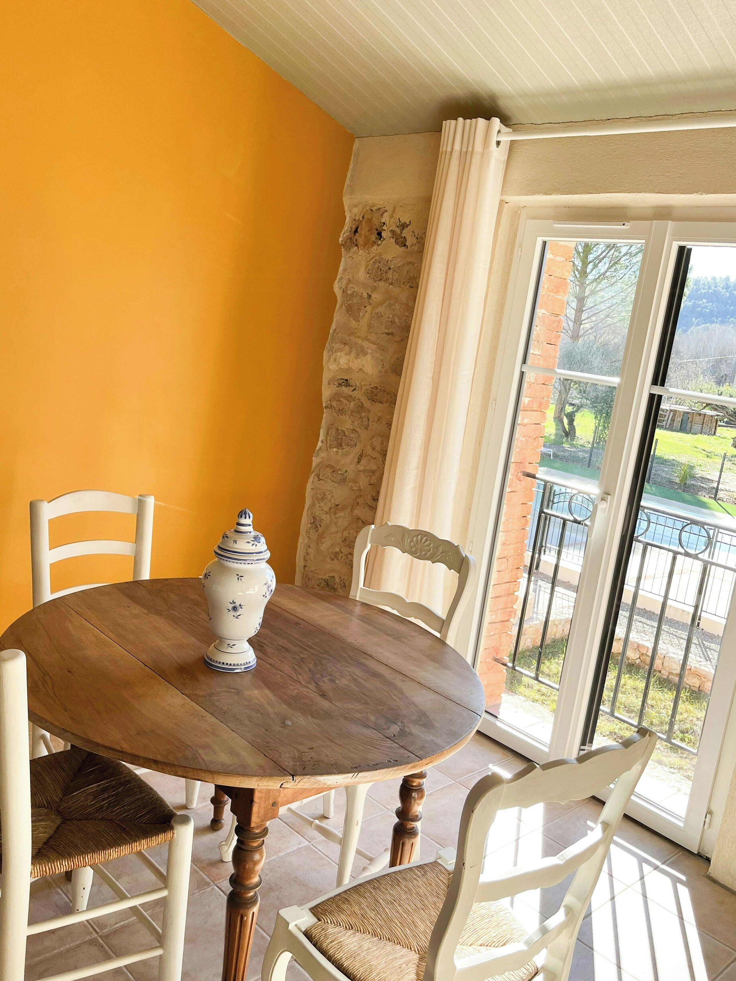 Un coin repas avec une table ronde en bois, des chaises blanches et un pichet en céramique blanche.
