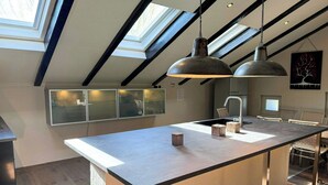 Una cucina moderna con lucernari, un'isola centrale e una zona pranzo con sedie in vimini.