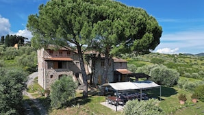A stone house with a large tree in front, outdoor seating, and a covered patio. - Large country house near Lucca with private pool (San Gennaro)