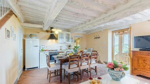 A dining area with a table set for four, wooden chairs, a white cabinet, and a television on a wooden stand. - Large country house near Lucca with private pool (San Gennaro)