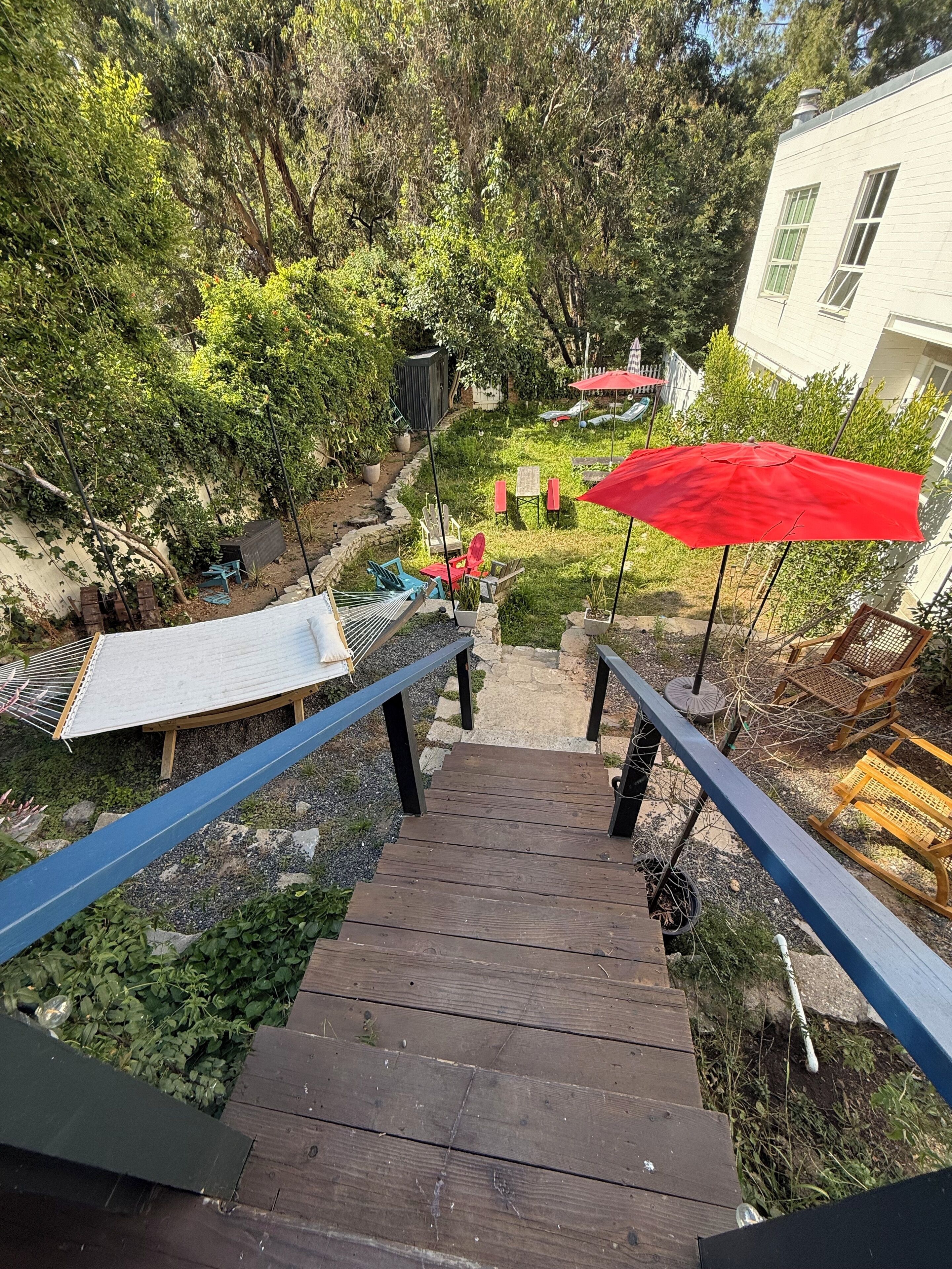 A wooden staircase leading to a garden area with outdoor furniture and umbrellas.
