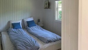 Et værelse med to senge, et lille bord, en vægmonteret hylde og et vindue.