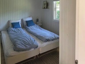 Ein Zimmer mit zwei Betten, einem kleinen Tisch, einem Wandregal und einem Fenster.