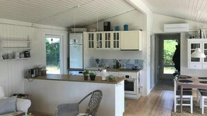Et moderne køkken med hvide skabe, en central ø og et spiseområde med en fletstol.