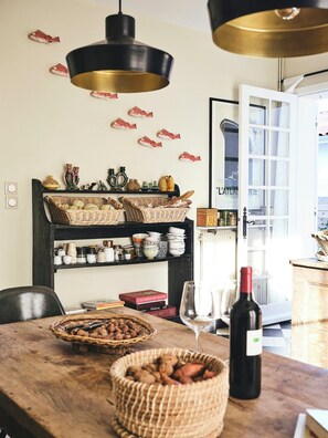 A dining area with a wooden table, wicker baskets, wine bottle, and a bookshelf with decorative items. - Family home between forest and ocean in Mimizan (Mimizan)