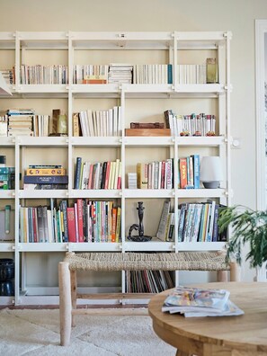 A bookshelf filled with books, a small table with a magazine, and a woven bench. - Family home between forest and ocean in Mimizan (Mimizan)