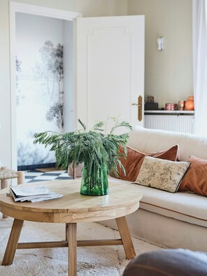 A living room with a round wooden table, a green vase with a plant, a beige sofa with brown cushions, and a white door in the background. - Family home between forest and ocean in Mimizan (Mimizan)