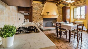 Una cocina con estufa a gas, pared de piedra, chimenea y comedor con mesa y sillas.