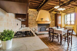 Eine Küche mit Gasherd, Steinwand, Kamin und Essbereich mit Tisch und Stühlen.