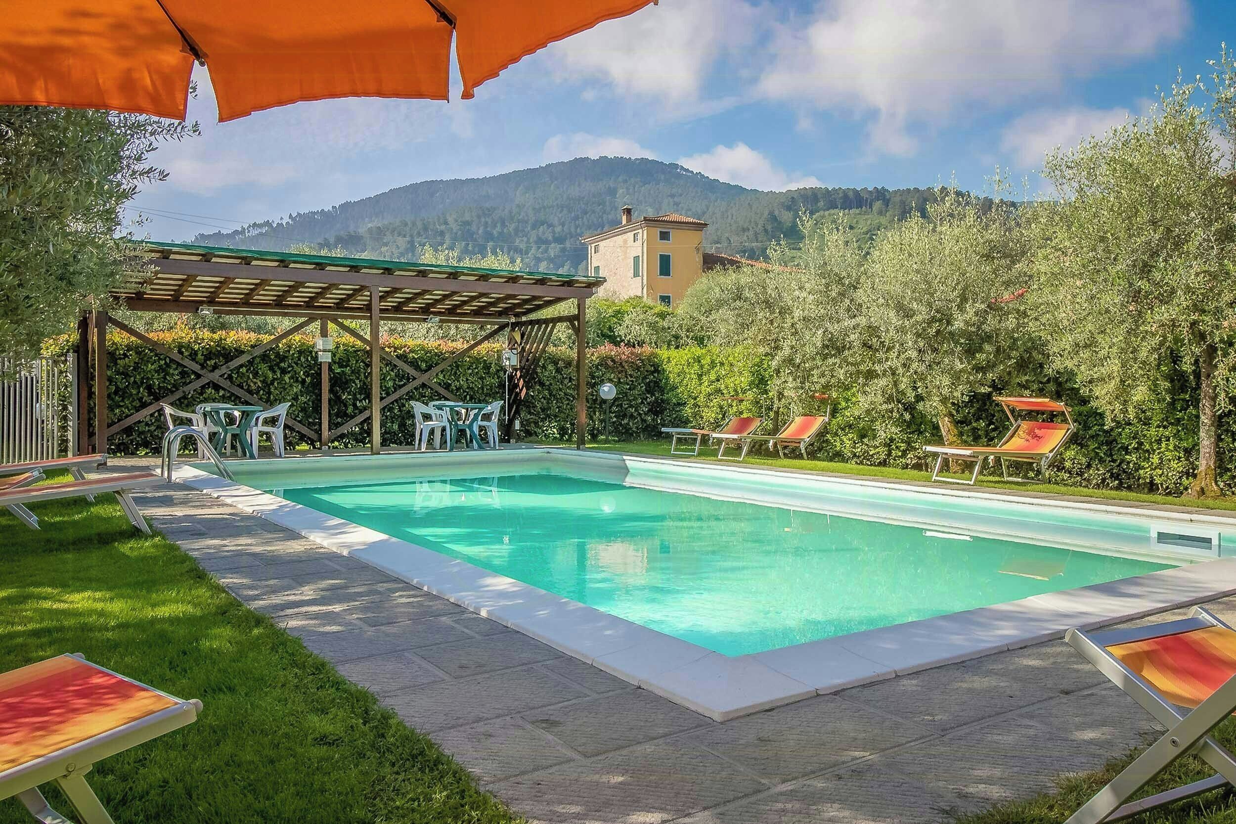 A swimming pool with lounge chairs, a pergola, and a mountain backdrop.