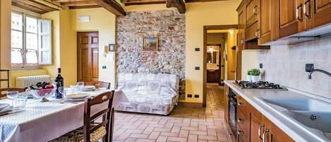 A rustic kitchen with wooden cabinets, a stone wall, and a tiled floor.
