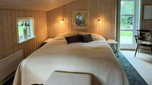 Een slaapkamer met een groot bed, een klein nachtkastje, een stoel en een raam met uitzicht op groen.
