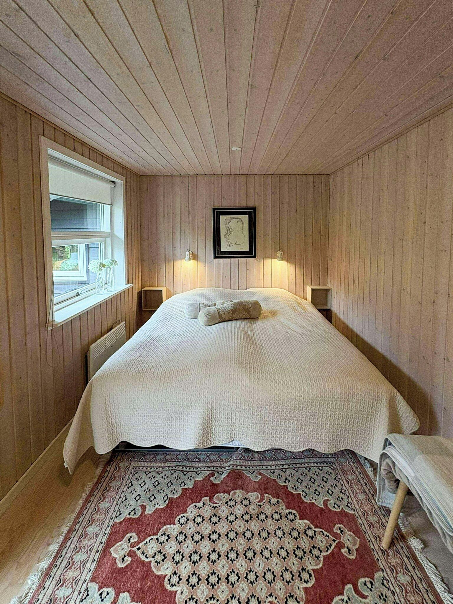 A bedroom with a large bed, wooden walls, a window with a view, and a framed picture on the wall.