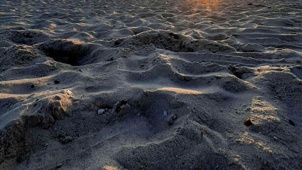 Een strand met golvende zandpatronen en een ondergaande zon op de achtergrond.